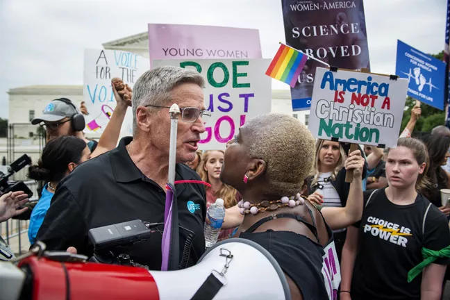 Demonstration utanför Högsta domstolen i Washington, USA. En abortmotståndare och en aborträttsförsvarare skriker på varandra. Bakom dem syns hbtq-flaggor, skyltar och plakat från båda sidor. 