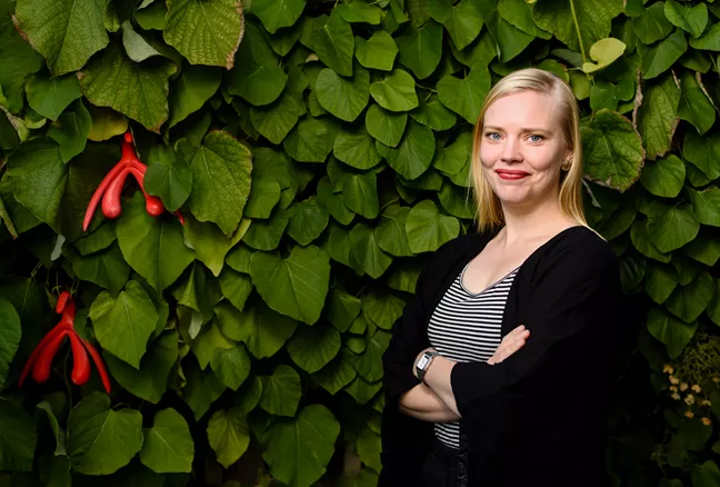 Jessica Påfs står framför ett grönt buskage. Bland bladen hänger två klitoris i plast. 